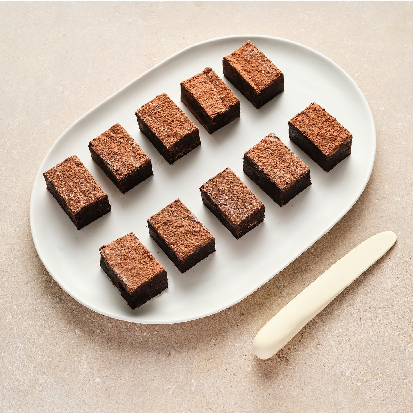A white plate containing ten rectangular chocolate brownies arranged in two rows