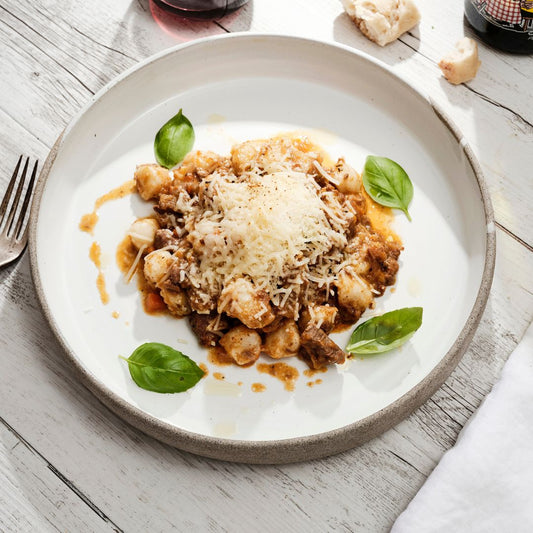 Plate of gnocchi with slow-cooked ragu sauce and parmesan cheese, garnished with basil leaves