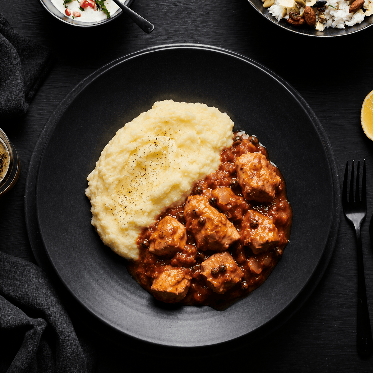 Black plate with mashed potatoes and syrian chicken dish