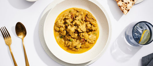 A plate of butter chicken served on a white plate with table settings