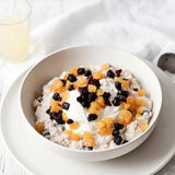 A bowl of Bircher Muesli topped with seasonal fruits and yogurt, served on a plate with a glass of milk in the background.