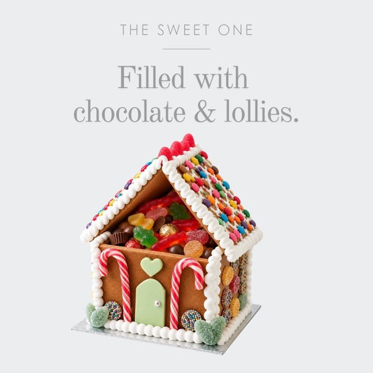 A gingerbread house-shaped candy treat on a light gray background with the text 'THE SWEET ONE' and 'Filled with chocolate & lollies.' Above the house are colourful candies and chocolate pieces visible through the roof, with white icing trim and candy canes on the front.