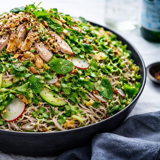 Salad with noodles, greens, and radishes in a black bowl on a table.