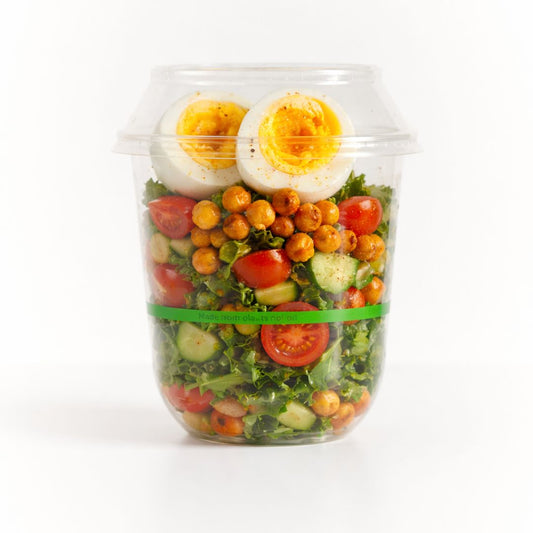 Salad with chickpeas, tomatoes, and boiled eggs in a clear container on a white background