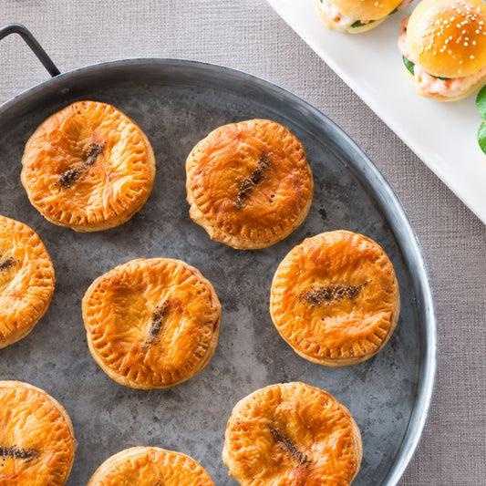 Round golden-brown baked chicken, leek & semillon mini pies with crimped edges sit on a dark metal baking pan