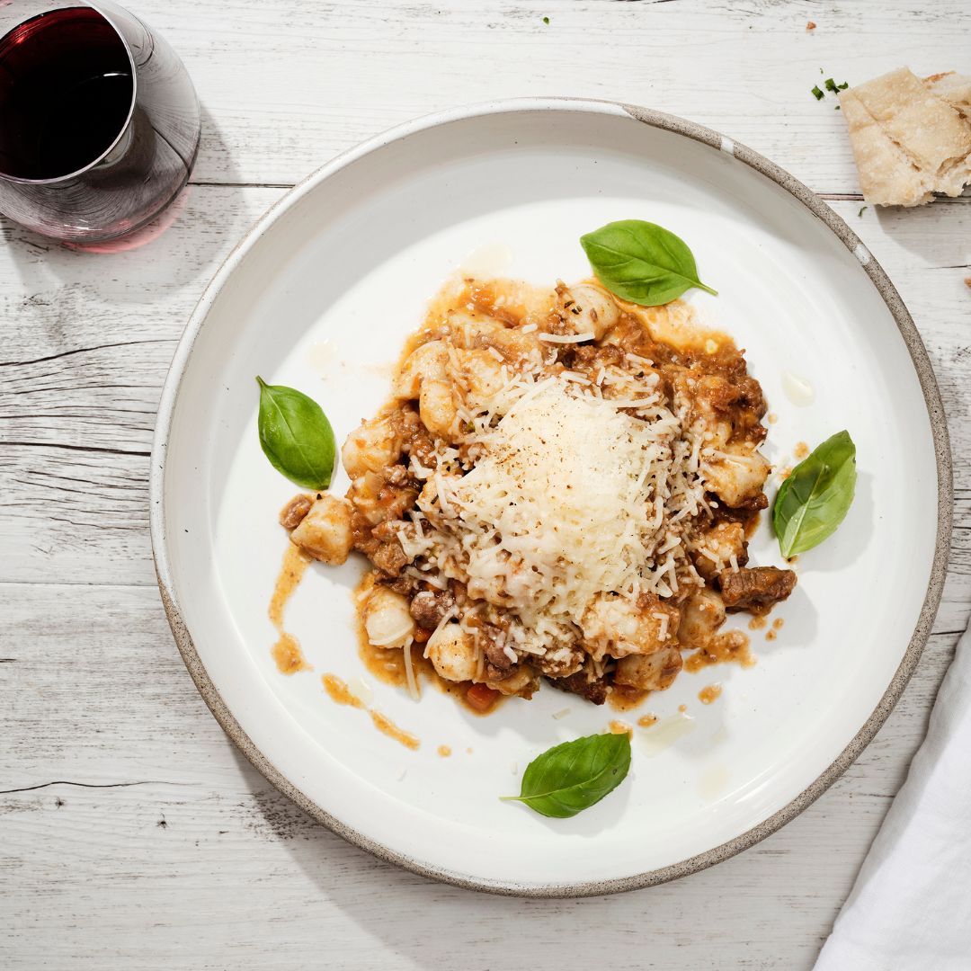 Plate of gnocchi with slow-cooked ragu sauce and parmesan cheese, garnished with basil leaves