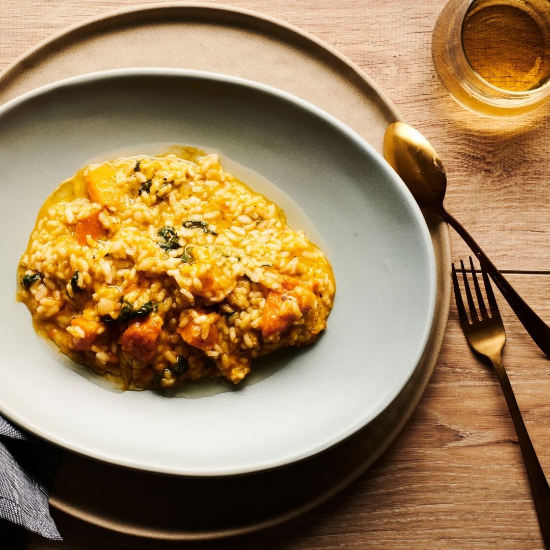 Pumpkin risotto on a light blue plate with gold spoon and fork on a wooden table