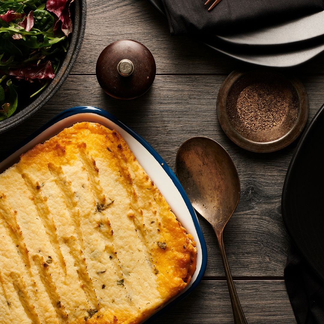 Shepherd's pie in a dish on a wooden table with a spoon