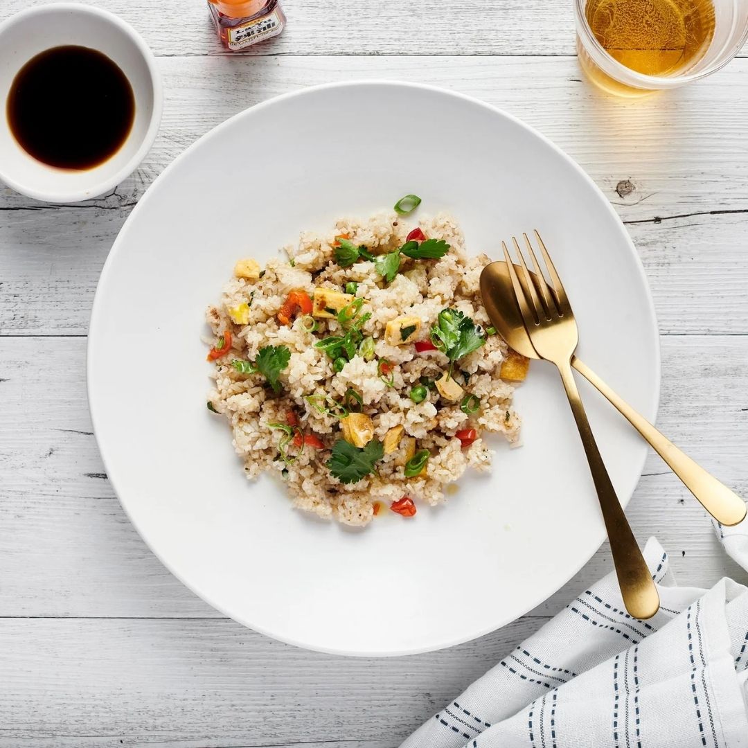 White plate with vegetarian fried rice a wooden table with a fork and soy sauce