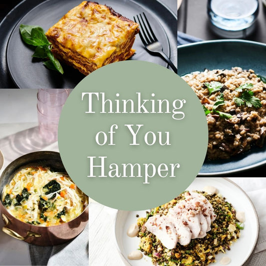 A collage of food dishes arranged around a large pale green circle with the text 'Thinking of You Hamper' in white. The dishes include a slice of layered lasagne, a bowl of poached chicken & grain, a copper pot of chicken & noodle soup, a plate of seasonal vegetarian risotto.