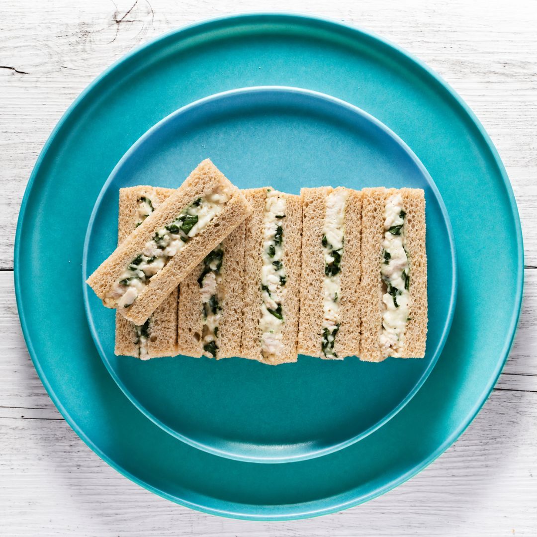 6 waldorf chicken finger sandwich slices filled with chicken and green herbs, arranged on a teal plate over a white wood surface.